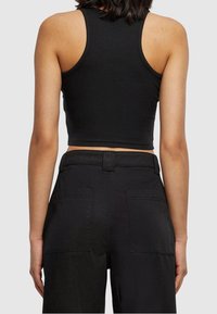 Svart kort tanktopp i ribbat material, med breda axelremmar och en figursydd design. Bärs med högmidjade svarta byxor med fickor.