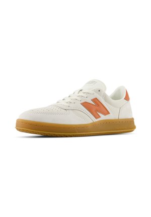 Zapatilla de ante blanco con detalles en naranja, con cordones redondos y suela de goma. El diseño incluye perforaciones para ventilación.