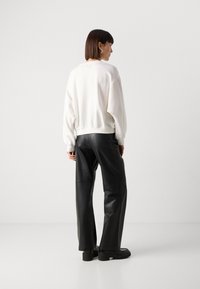 Felpa bianca con una vestibilità comoda e polsini a coste, abbinata a pantaloni in pelle nera a vita alta con una texture liscia e gamba larga.