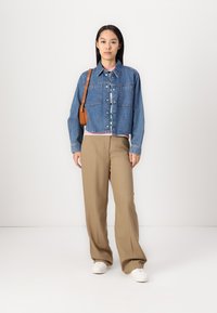 Džínová bunda s prednými vreckami, zapínaním na gombíky a golierom. Spárované s béžovými širokými nohavicami a bielymi teniskami. Hnedá crossbody taška.