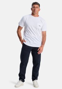 Witte katoenen t-shirt met korte mouwen en een borstzak, gecombineerd met donkerblauwe broek en witte sneakers. Schone, casual look.