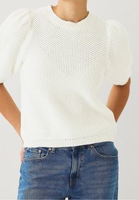Maglione bianco a maniche corte lavorato a maglia con pattern testurizzato e colletto e orlo a coste. Abbinato a jeans in denim blu.