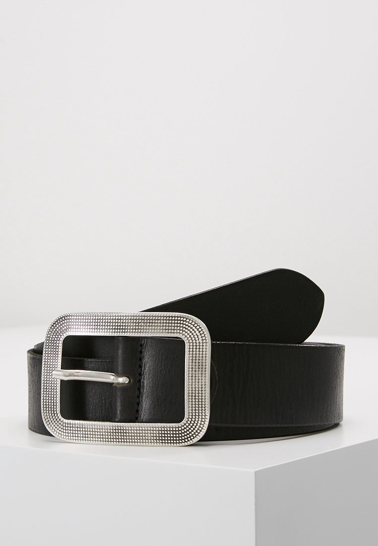 Ceinture en cuir noir avec une grande boucle rectangulaire argentée texturée, présentée enroulée sur une surface blanche sur fond gris clair.