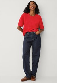 Rød kortærmet striktrøje parret med høj talje mørkeblå jeans og brune mokkasiner. Outfittet har et afslappet snit.