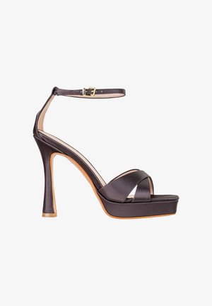 Sandalo nero in raso con tacco alto e plateau, sottile cinturino alla caviglia, fibbia dorata e cinturini frontali incrociati su sfondo bianco.