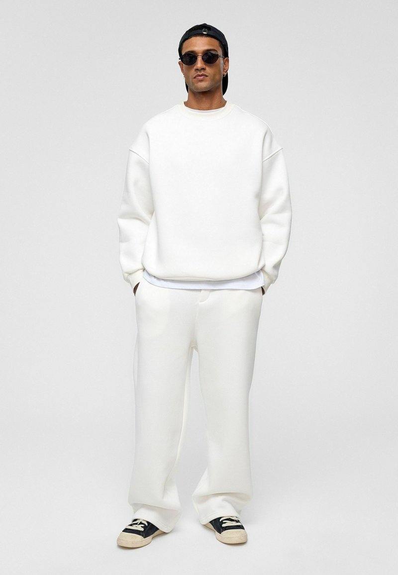 Witte sweatshirt en trainingsbroek set, met een ontspannen pasvorm, zachte textuur en een minimalistisch ontwerp. Gecombineerd met zwarte zonnebril.