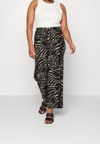 Gestreepte wijde broek in zwart met beige zebra-prints, met een elastische tailleband. Gecombineerd met een witte mouwloze top en zwarte sandalen.