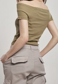 Top off-the-shoulder ribbed verde oliva abbinato a pantaloni cargo grigio chiaro con tasche a pattina, texture liscia e silhouette aderente.