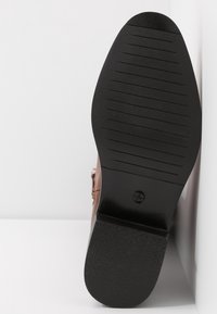 Chaussure en cuir marron à surface lisse, semelle en caoutchouc noire plate avec des rainures horizontales et design à bout rond.