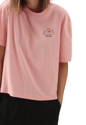 Personne portant un T-shirt ample Vans rose avec un petit logo de palmier et le texte « Off The Wall » sur la partie supérieure gauche de la poitrine.
