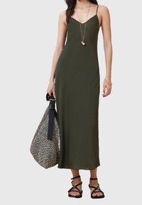 Olivgrön maxiklänning med tunna axelband och V-ringning. Kombinerad med en mönstrad väska och svarta sandaletter med remmar.