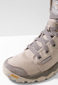 Beige vysoké boty vyrobené z textilu a semiše, se šedými šňůrkami, kovovými očky a robustní podešví Vibram pro lepší přilnavost.