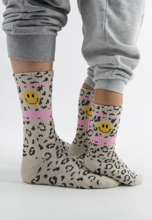 Kniestrümpfe mit Leopardenmuster in Beige, pinken Streifen und gelben Smiley-Akzenten, aus einem weichen, strukturierten Material gefertigt.