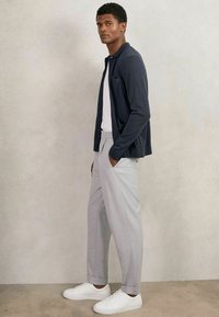 Cardigan azul marino con botones, camiseta blanca, pantalones de cuadros grises, zapatillas blancas. Textura suave, corte ajustado, bolsillo visible en el cardigan.