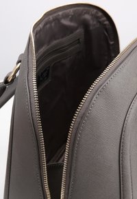 Borsa a tracolla grigia con texture, dotata di apertura con zip, caratterizzata da hardware beige e una tasca interna. Finitura liscia con forma strutturata.