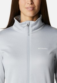 Hellgraue Zip-Jacke mit Stehkragen, ausgestattet mit einer strukturierten Oberfläche und dem Columbia-Logo auf der linken Seite.