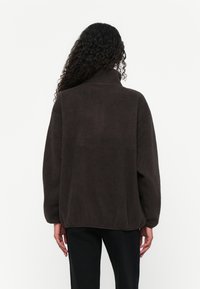 Donkerbruine fleece pullover met een hoge kraag, verlaagde schouders en geribbelde zoom. Textuur met een zachte, gezellige uitstraling.