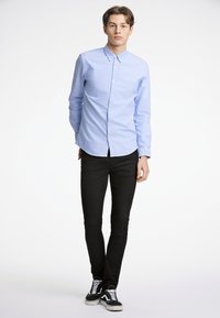 Camicia azzurro chiaro con bottoni, jeans neri slim-fit e sneakers bianco e nero. La camicia presenta una texture liscia e un design classico del colletto.