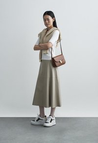 Beige leather midi skirt, fitted white top, knitted beige sweater draped over shoulders, brown crossbody bag, white and black sneakers.