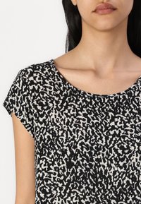Camiseta de algodón con cuello redondo y mangas cortas, que presenta un patrón abstracto en blanco y negro sobre un fondo claro.