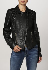 Giacca in pelle nera con colletto strutturato, pannelli testurizzati e tasche con cerniera, caratterizzata da un design aderente e una leggera lucentezza.