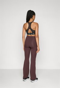 Top desportivo preto com costas recortadas e faixa elástica com a marca, combinado com leggings largas cor bordô. Ténis pretos completam o conjunto.