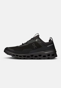 Chaussure de sport noire avec une tige en maille texturée, un talon moulé et une semelle à motifs proéminents avec des découpes pour un soutien léger.