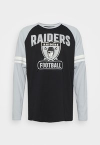 Langarmshirt mit schwarzem Körper und grauen Ärmeln, mit dem Text "RAIDERS", einer Fußballgrafik und zwei weißen Streifen an den Ärmeln.