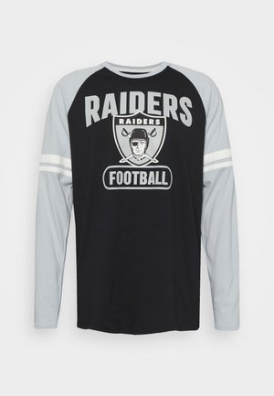 Chemise à manches longues avec un corps noir et des manches grises, présentant le texte "RAIDERS", un graphique de football et deux rayures blanches sur les manches.