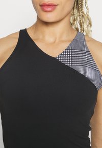 Top da donna nero con un design asimmetrico e una sezione a fantasia in bianco e nero. Texture liscia e forma attillata.