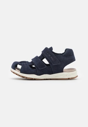 Sandale enfant bleu marine avec brides ajustables, bout fermé, maintien de la cheville rembourré et semelle en caoutchouc blanche.