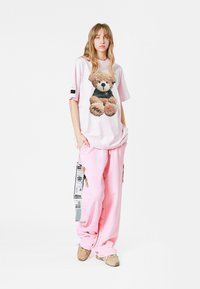 Camiseta rosa de gran tamaño con un gráfico de un oso de peluche, combinada con pantalones de chándal rosas sueltos que cuentan con bolsillos laterales y detalles en negro.