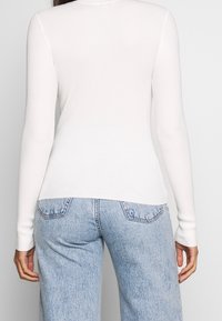 Vit ribbad långärmad topp med hög krage, parat med ljusblå högmidjade jeans med bakfickor och en urblekt textur.