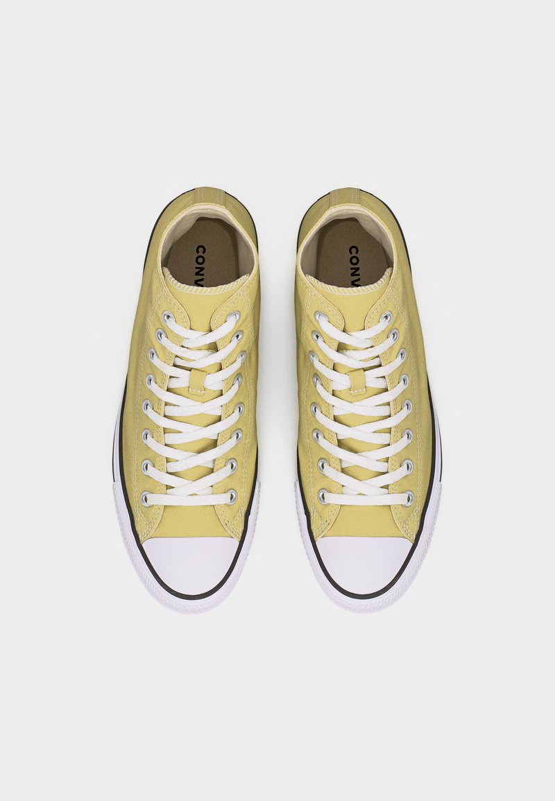 Par de zapatillas bajas de lona amarillas con punteras de goma blancas y cordones blancos, vistas desde arriba sobre un fondo blanco.