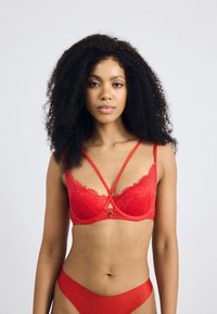 Red lace bra with sheer underwire, scalloped edges, and decorative strapping. Matching red bikini bottom features a smooth texture.
