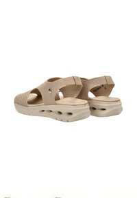 Sandalias de tela beige con parte superior texturizada, talón abierto y correas ajustables. La suela acolchada cuenta con orificios de ventilación para mayor transpirabilidad.