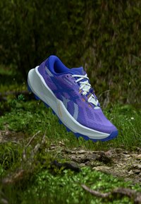 Chaussure de trail running violette avec une tige en mesh respirant, des motifs texturés et une grande semelle intermédiaire blanche. Elle est dotée d'une semelle extérieure robuste pour une meilleure adhérence.