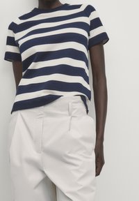 Navy and white striped knit top with short sleeves, round neckline, paired with light-colored, pleated trousers. Smooth texture.