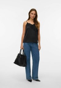 Czarny satynowy top na ramiączkach z koronkową lamówką, zestawiony z szerokimi niebieskimi dżinsami. Modelka niesie czarną skórzaną torebkę.