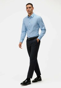 Lichtblauw overhemd met knoopsluiting en een getailleerde pasvorm, gecombineerd met donkere broek en zwarte schoenen. Glad stof met een subtiele glans.