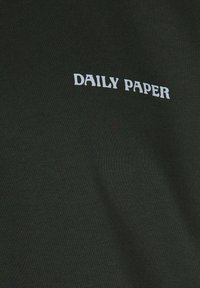 Mørkegrøn bomulds skjorte med teksten "DAILY PAPER" i hvidt henover brystet, teksturen er glat med ribbet finish.
