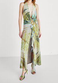 Maxiklänning i mjuk, blommönstrad tyg med djup v-ringning, draperad design, volangdetaljer och guldaccent i midjan. Gröna sandaler med remmar.