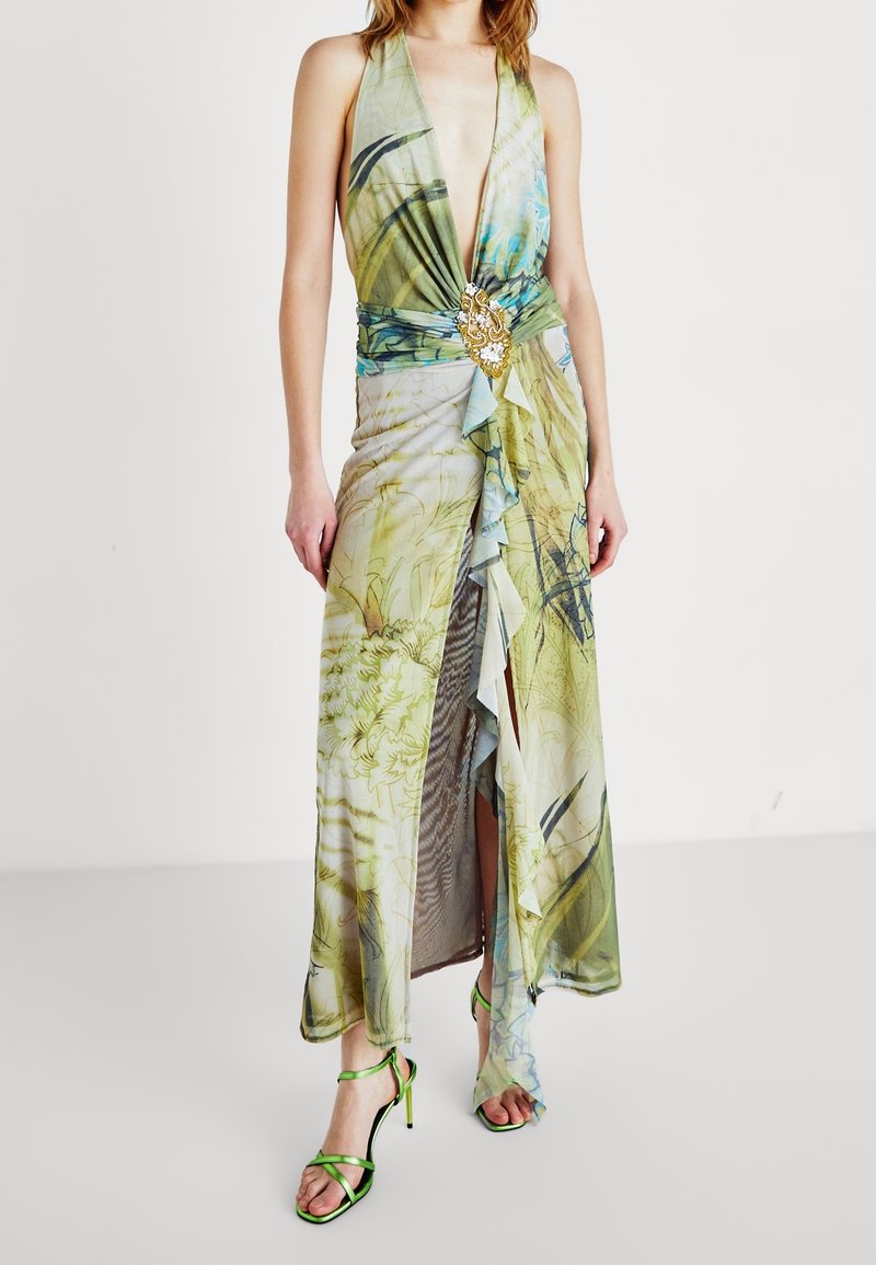 Maxiklänning i mjuk, blommönstrad tyg med djup v-ringning, draperad design, volangdetaljer och guldaccent i midjan. Gröna sandaler med remmar.