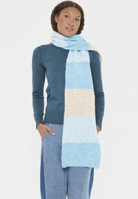 Világoskék és krémszínű csíkos sál, puha, texturált kötött anyagból, laza stílusban, egy modell nyakán elhelyezve, kényelmes és casual megjelenéssel.