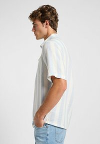 Camicia a maniche corte a righe azzurre e bianche, con tasca, realizzata in tessuto leggero, dalla vestibilità comoda e colletto standard.