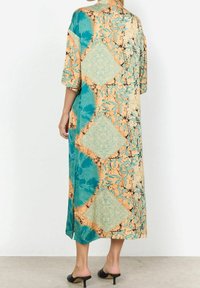 Pitkä kuvioitu mekko turkoosilla, beigen ja oranssin sävyillä. Mukana löysä malli, lyhyet hihat ja keskipitkä helma. Sileä kangas.