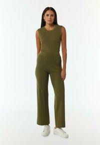 Olijfgroene geribbelde mouwloze top en bijpassende wijde broek; zachte textuur; discreet zijvak; gecombineerd met witte sneakers.