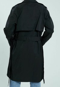 Czarny płaszcz trench z paskiem w talii, warstwowym tyłem i gładką teksturą. Zawiera epoletki na ramionach oraz średnią długość.