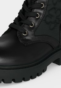 Botte en cuir noir à lacets avec œillets métalliques, panneau latéral matelassé et semelle épaisse à crampons.