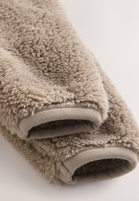 Tissu beige duveteux avec une surface texturée et pelucheuse, équipé de poignets gris lisses. Doux, chaud, idéal pour des vêtements confortables.